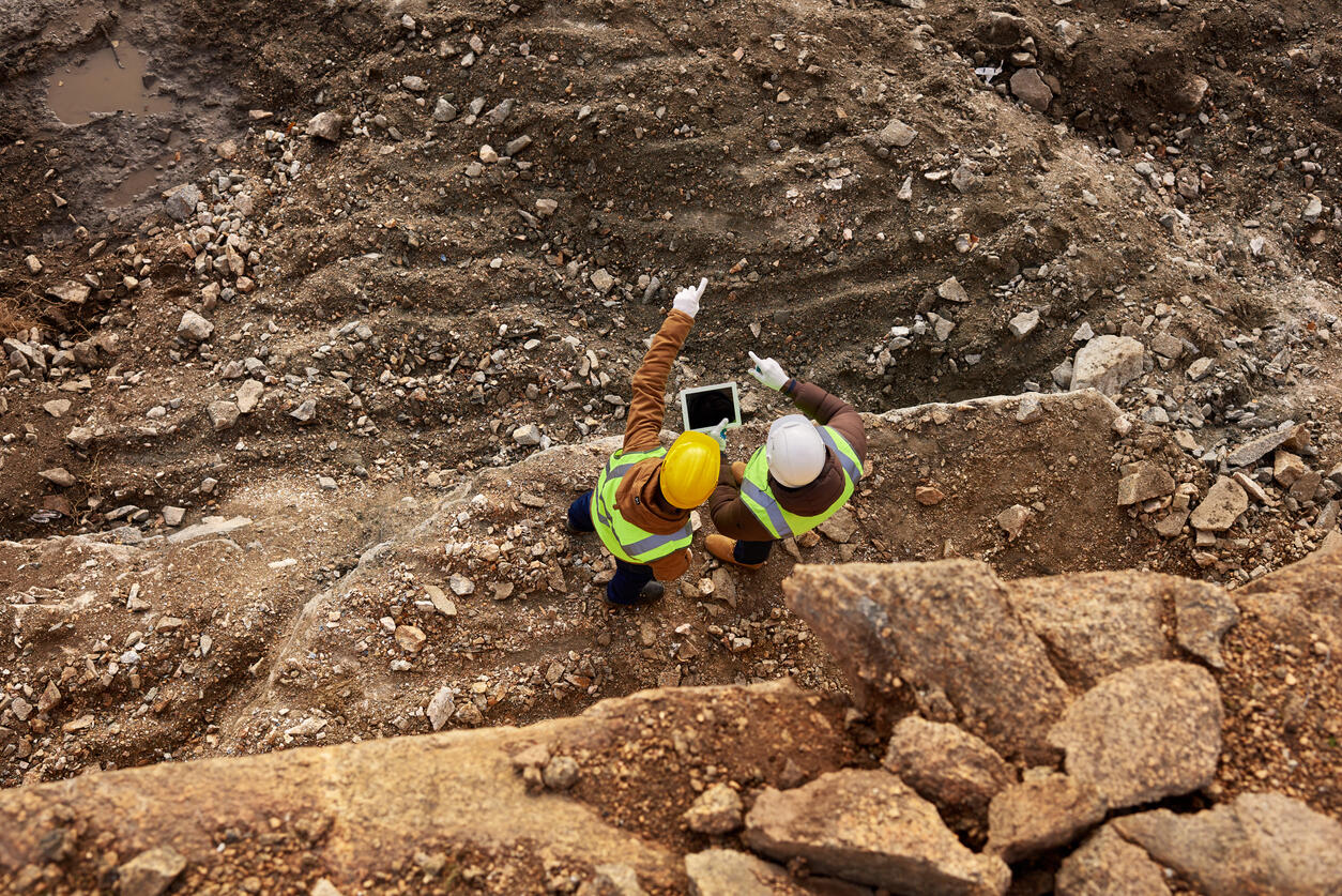 Top view shot of two industrial workers wearing reflective jackets standing on mining worksite outdoors using digital tablet
